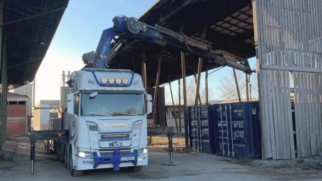 Wold Kran & transport AS på løfteoppdrag. Kranbilen står plassert ved noen containere.