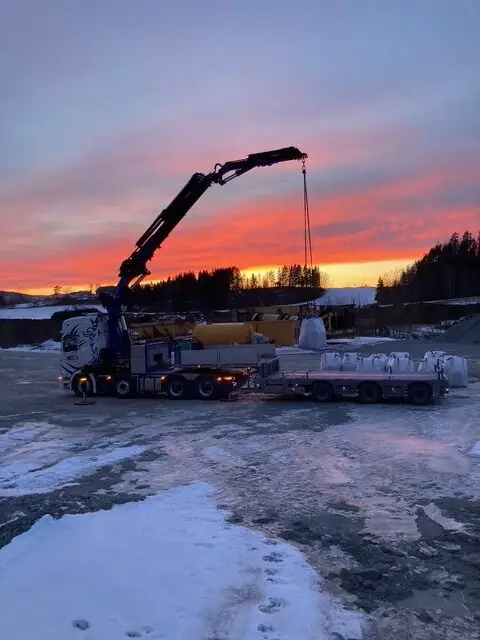 Wold Kran & transport AS på oppdrag med å transportere sandsekker under soloppgang på snø- og isdekket føre.