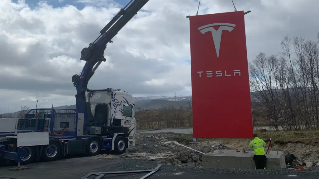 Wold Kran & transport AS på plass med kranbilen som løfter et Tesla-skilt på plass.